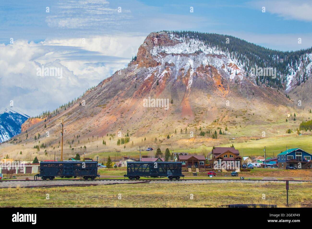 Train cars on track in front of houses in Silverton Colorado with mountains with snow in background. Stock Photo