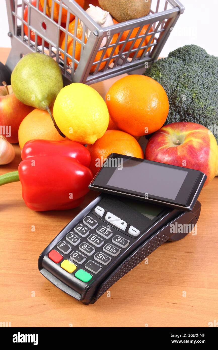 Payment terminal, credit card reader with mobile phone with NFC technology and fresh fruits and vegetables with plastic shopping carts, cashless payin Stock Photo