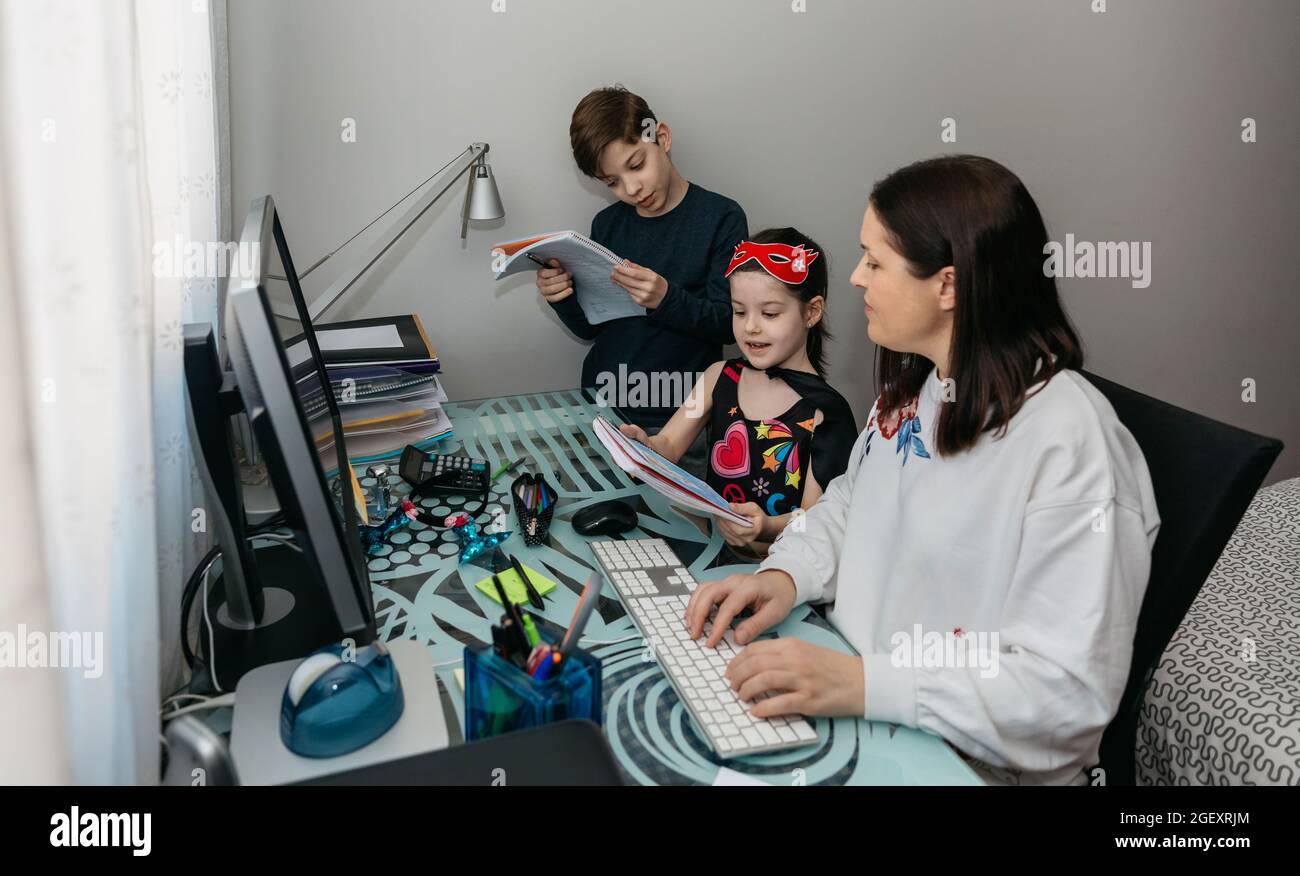 Woman teleworking and reviewing her children's homewor Stock Photo