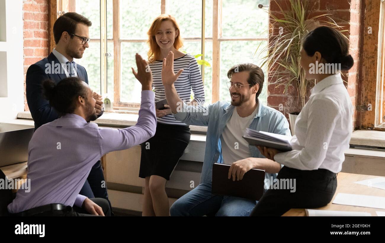 Multiracial employees giving high five during group briefing in office ...
