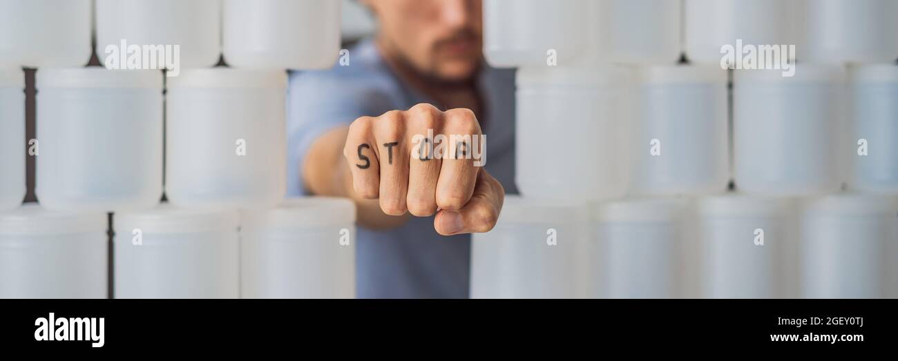 BANNER, LONG FORMAT Man showing stop surrounded by many jars of yoghurt that he uses in a year. A huge amount of plastic food jars. Excessive Stock Photo