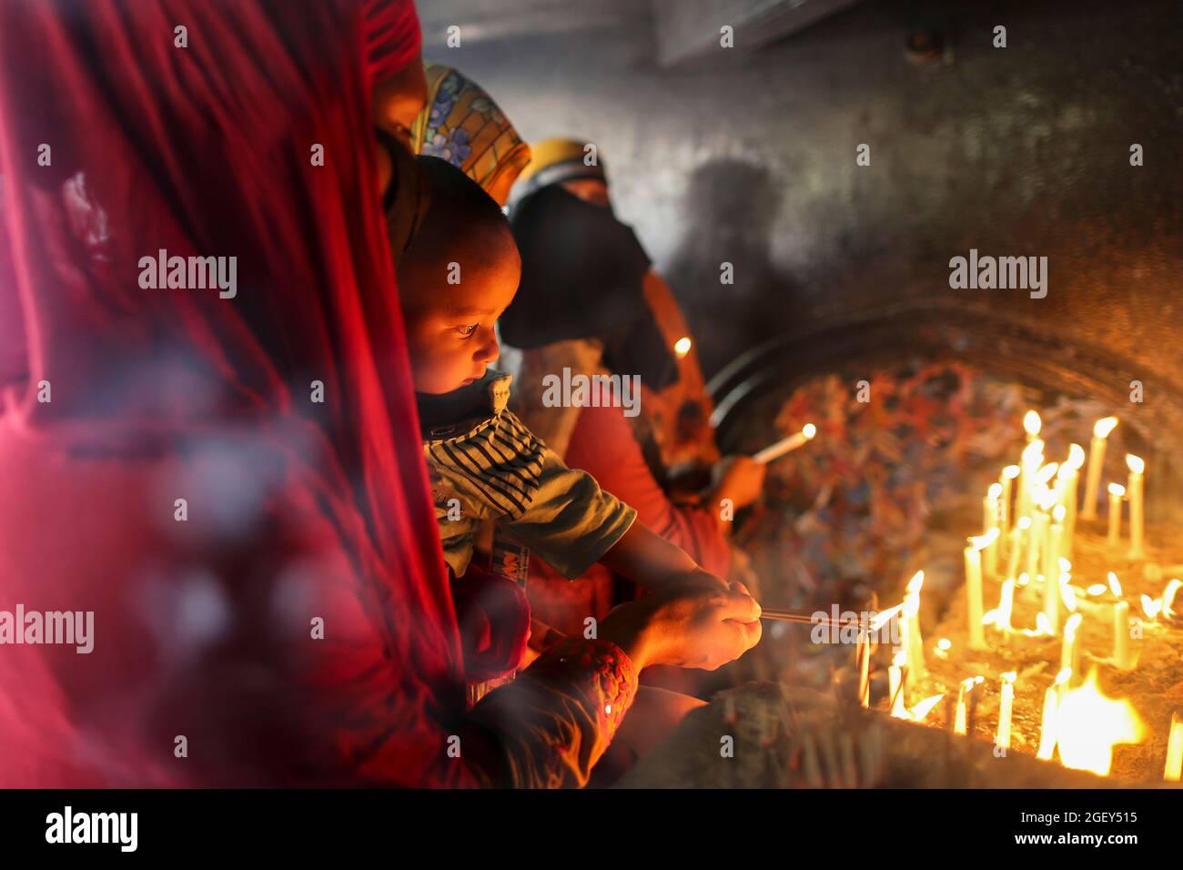 DHAKA, BANGLADESH, AUGUST 20: A Shia muslim woman holds ababy while  lights a candle and pray for imam hussain, at Husani-dalan. Musilm People take part during  a religious procession in the month of Muharram on the occasion to commemorate  Ashura Day. Ashura is the tenth day of Muharram, the first month of the Islamic calendar commemorating the martyrdom of Imam Hussein, the grandson of the Prophet hazrat Muhammad. On August 20, 2021 in Dhaka, Bangladesh. Stock Photo