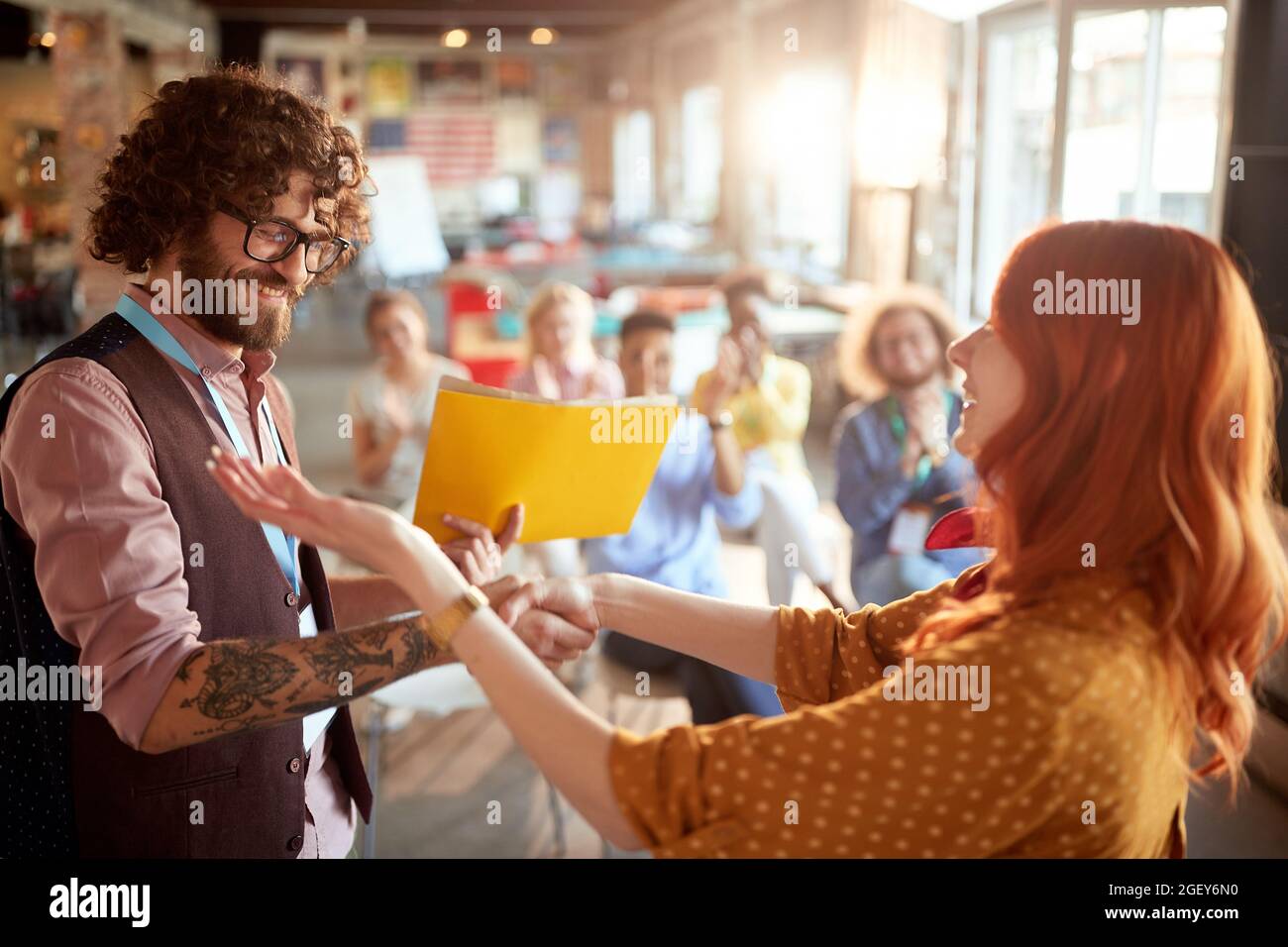 young redhead female congratulate to a caucasian business student after successful attending seminar, giving him certificate in folder. selective focu Stock Photo
