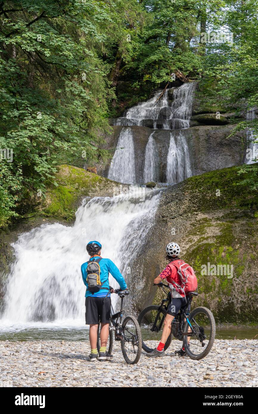 young happy grandmother and her grandson underway with their electric Mountainbikes in the Allgaeu Alps at a waterfall near Oberstaufen, bavarian Alps Stock Photo