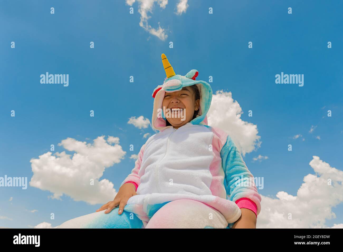 A closeup shot of a happy Hispanic boy in a unicorn costume and blue sky on the background Stock Photo