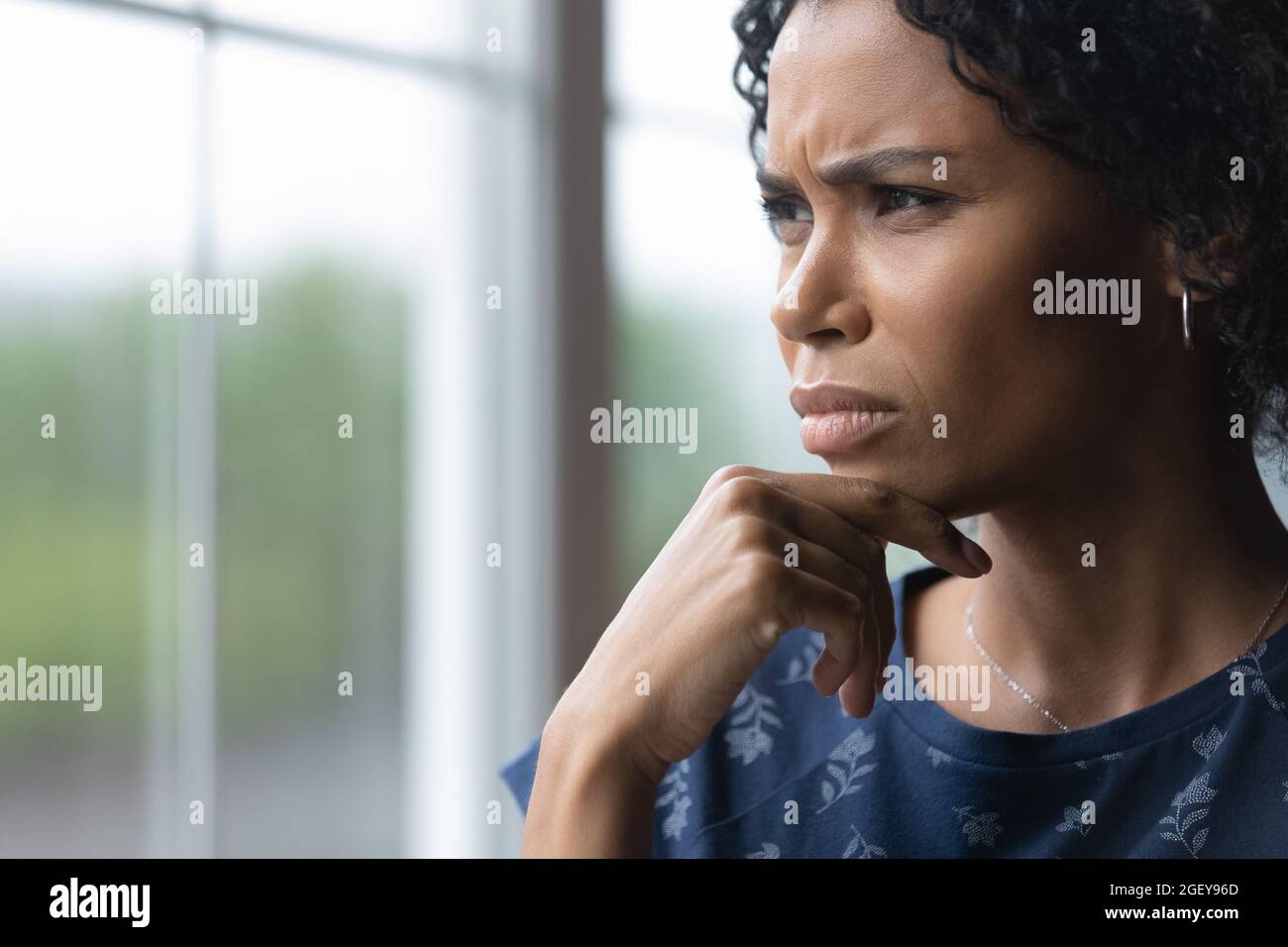 Frustrated concerned millennial African American woman looking out of window Stock Photo