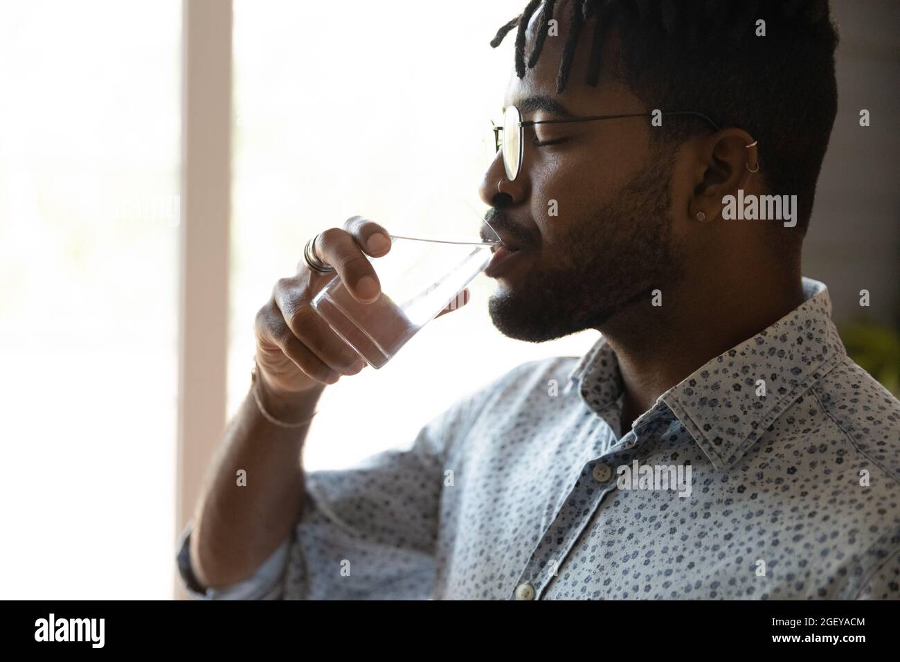 Peaceful millennial Afro American guy drinking water with closed eyes Stock Photo