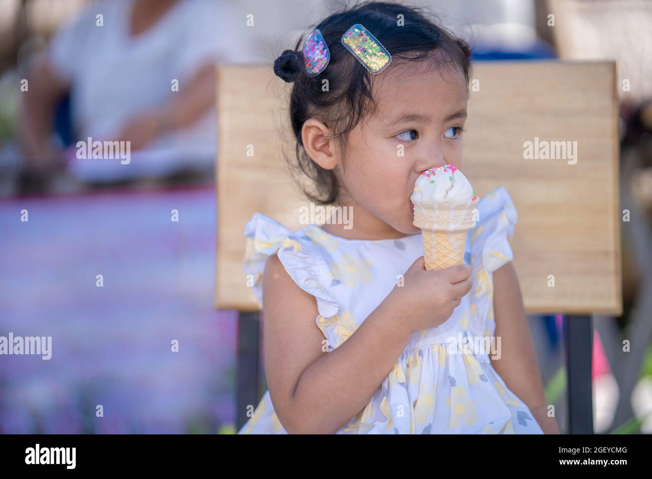 The cute little girl sitting on a wooden chair eating soft ice cream ...