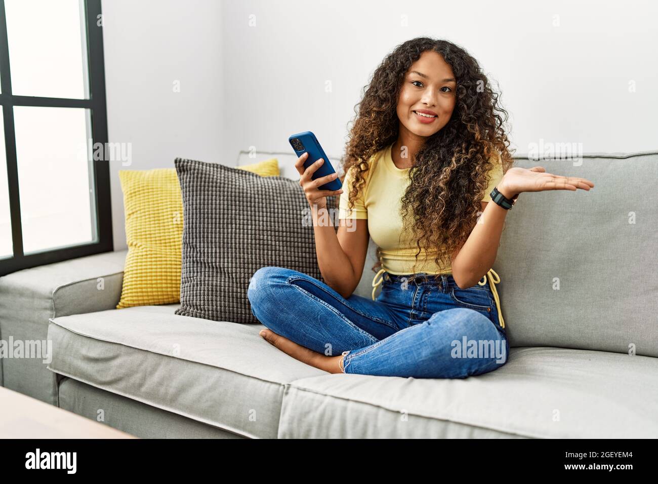 Beautiful hispanic woman sitting on the sofa at home using smartphone ...