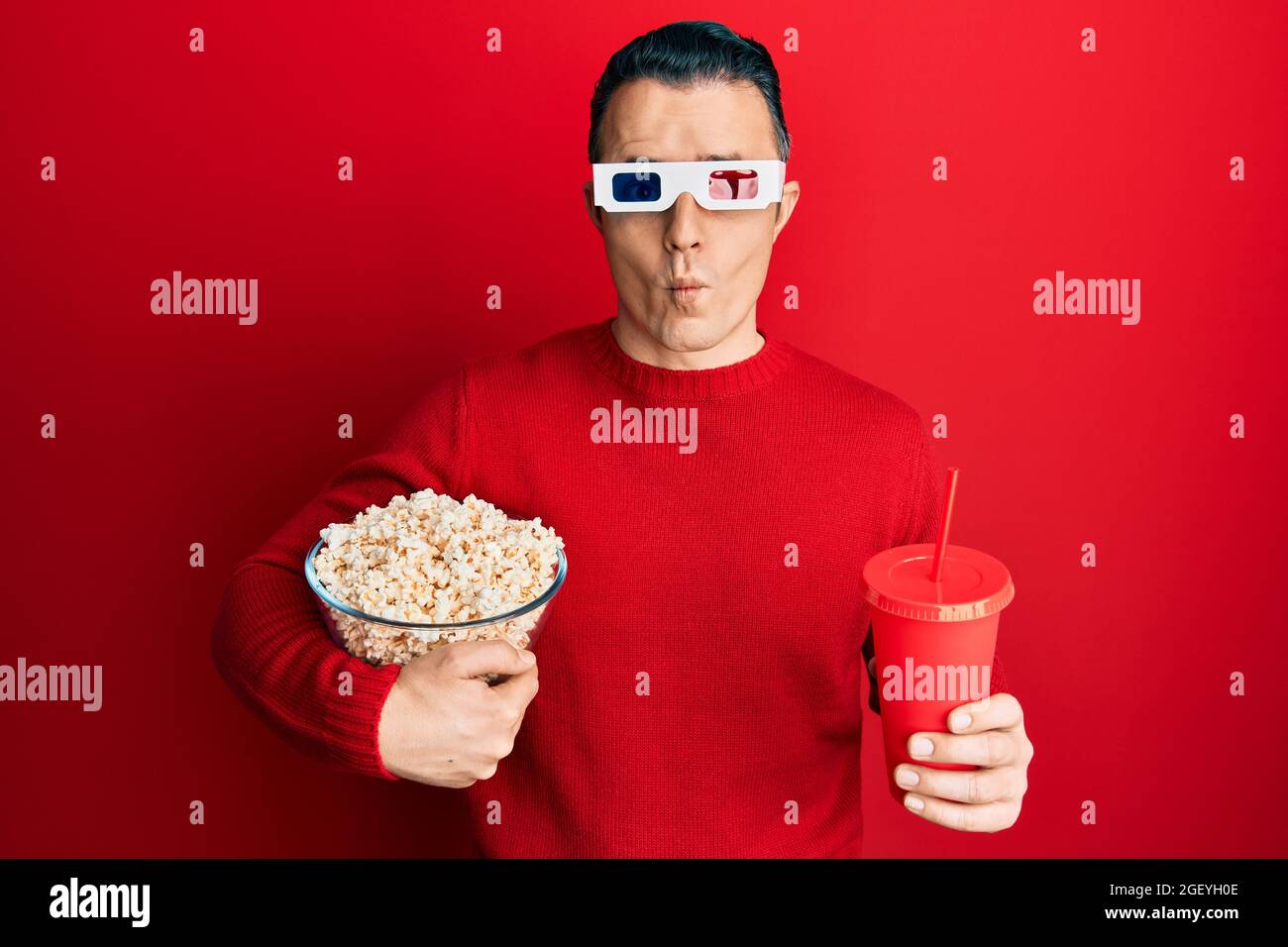 Handsome young man eating popcorn and soda wearing 3d glasses making fish  face with mouth and squinting eyes, crazy and comical Stock Photo - Alamy