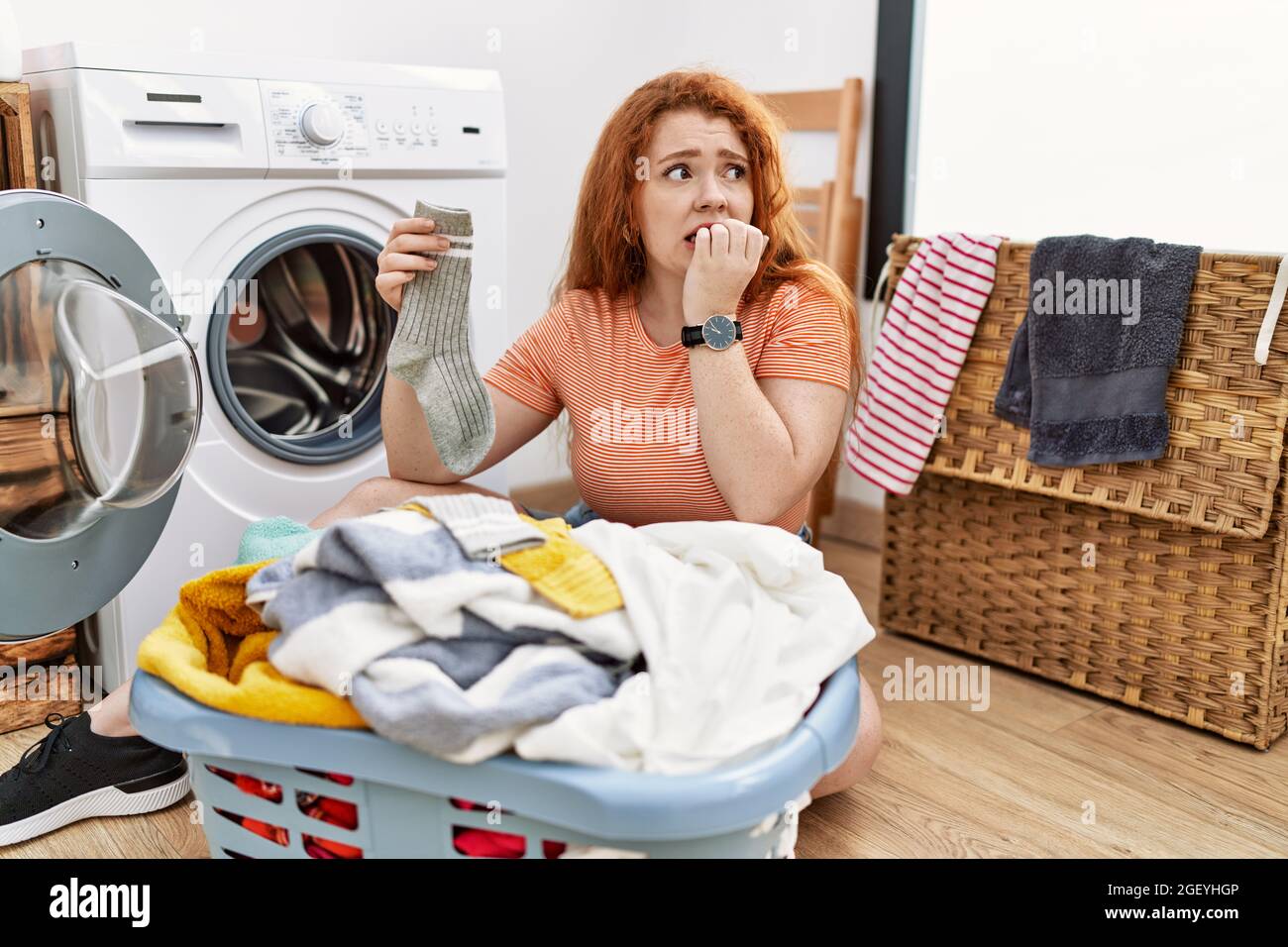 Young redhead woman putting dirty laundry into washing machine looking ...
