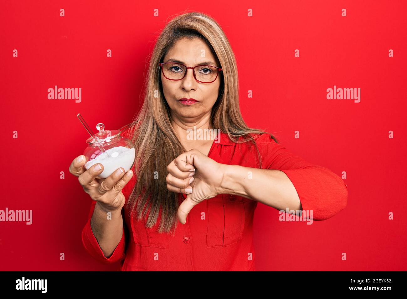 Middle age hispanic woman holding bowl with sugar with angry face ...