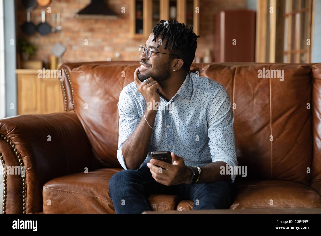 Thoughtful millennial African guy with mobile phone looking at window Stock Photo