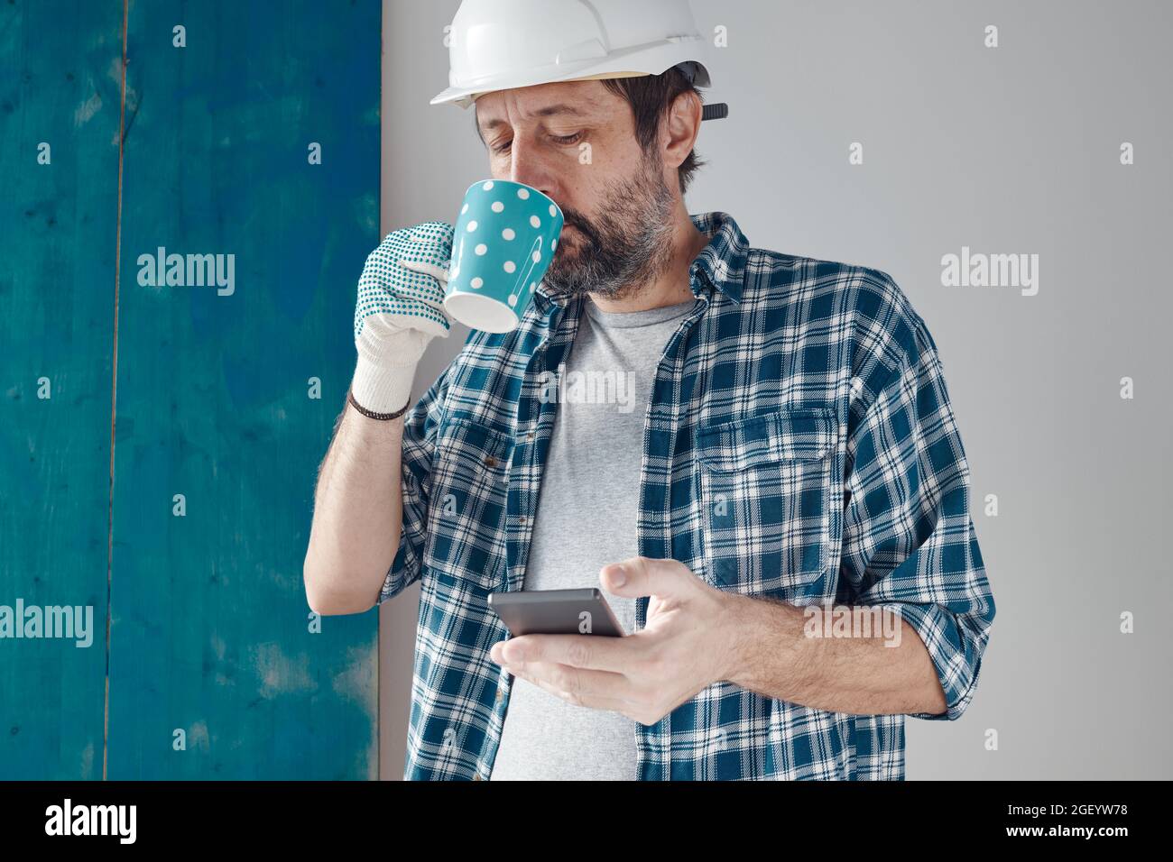 Construction engineer on a morning coffee break using mobile phone, relaxing and preparing for work Stock Photo