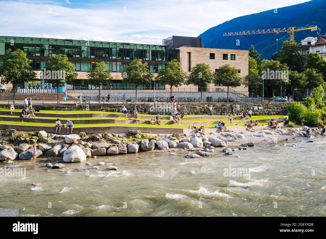 Merano, South Tyrol: Tourists relaxing at the banls of Passer River with the Therme spa in the background Stock Photo