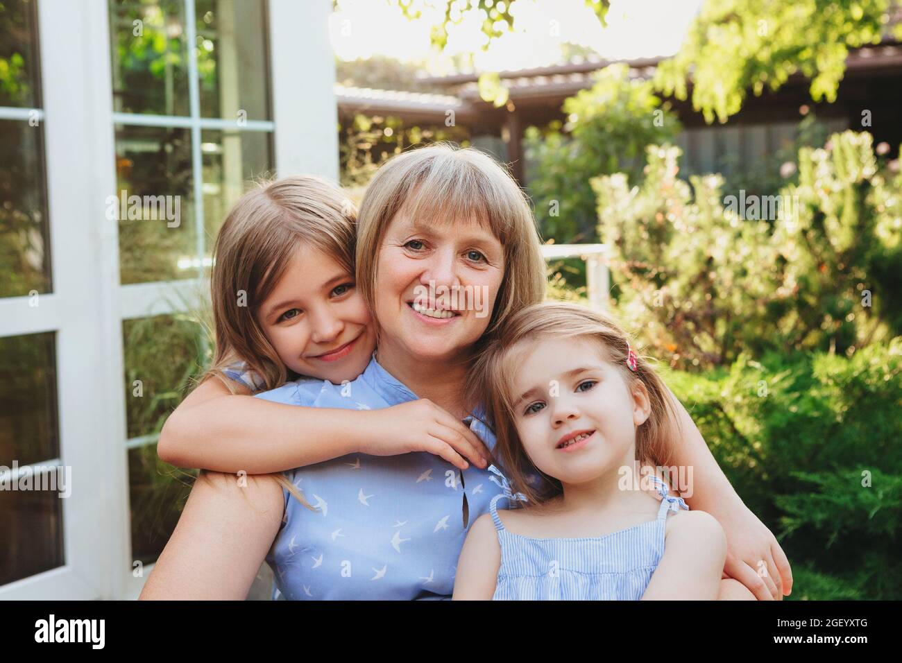 Happy loving middle-aged grandma hugging  granddaughters while standing in garden on summer day, grandmother with small girls spending time together i Stock Photo