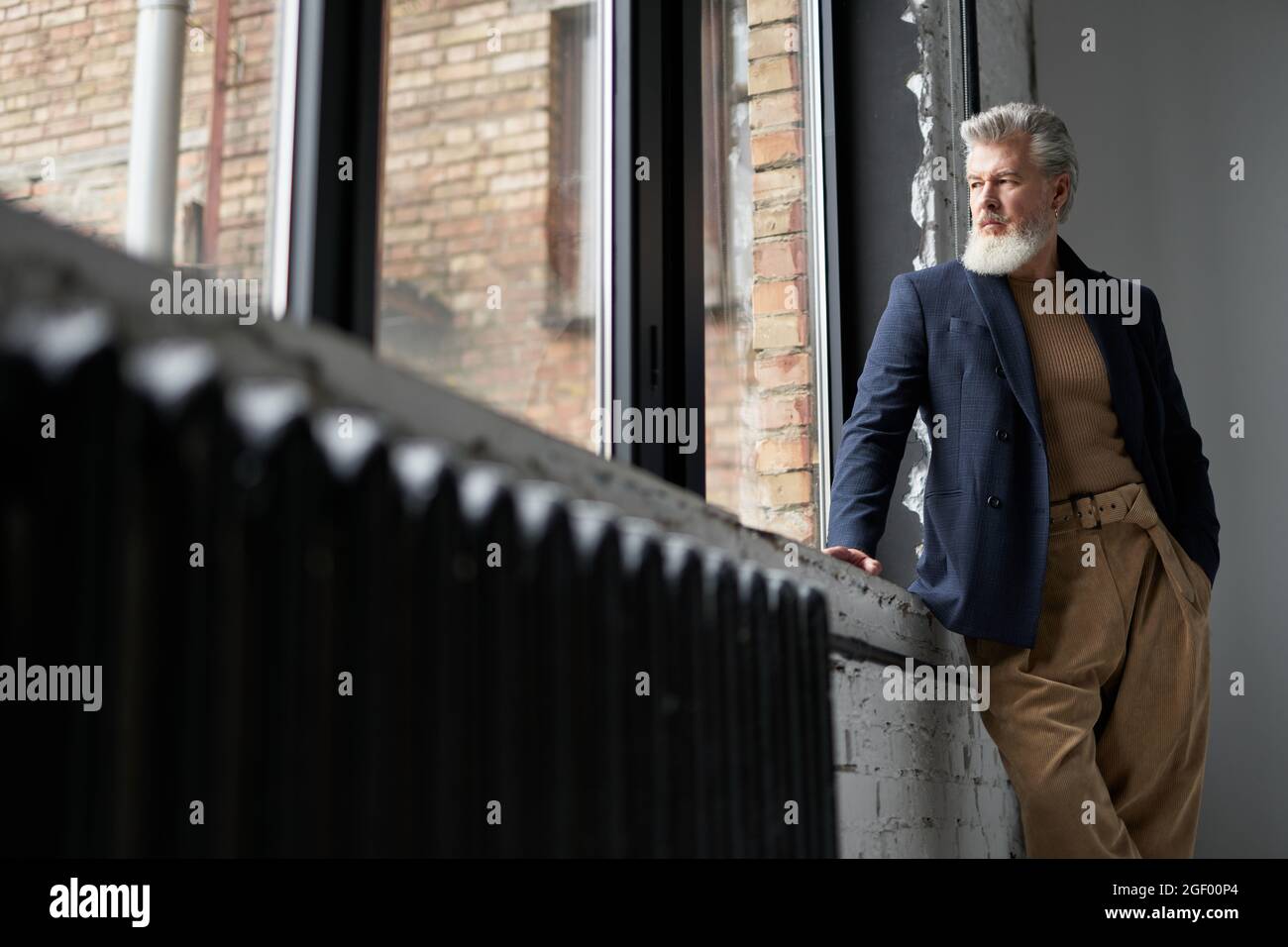 Stylish mature man in business casual wear looking out a large window,  being thoughtful while standing in loft interior Stock Photo - Alamy