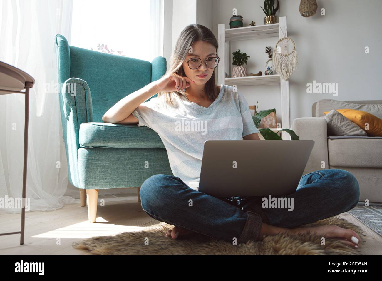 Young woman using laptop to work, sitting on the floor at home, Flexible hours and remote work Stock Photo