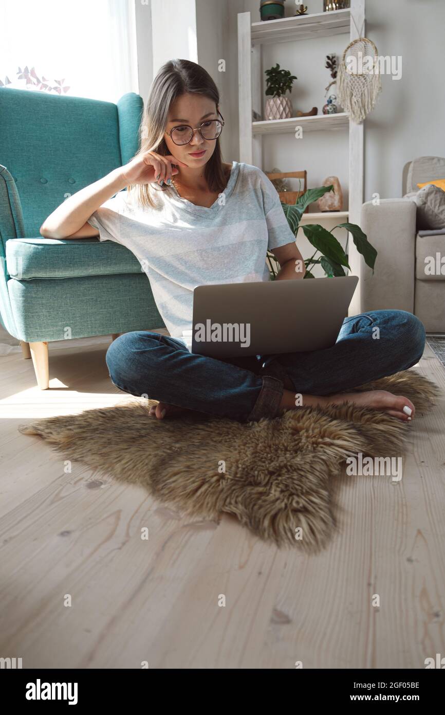 Young woman using laptop to work, sitting on the floor at home, Flexible hours and remote work Stock Photo