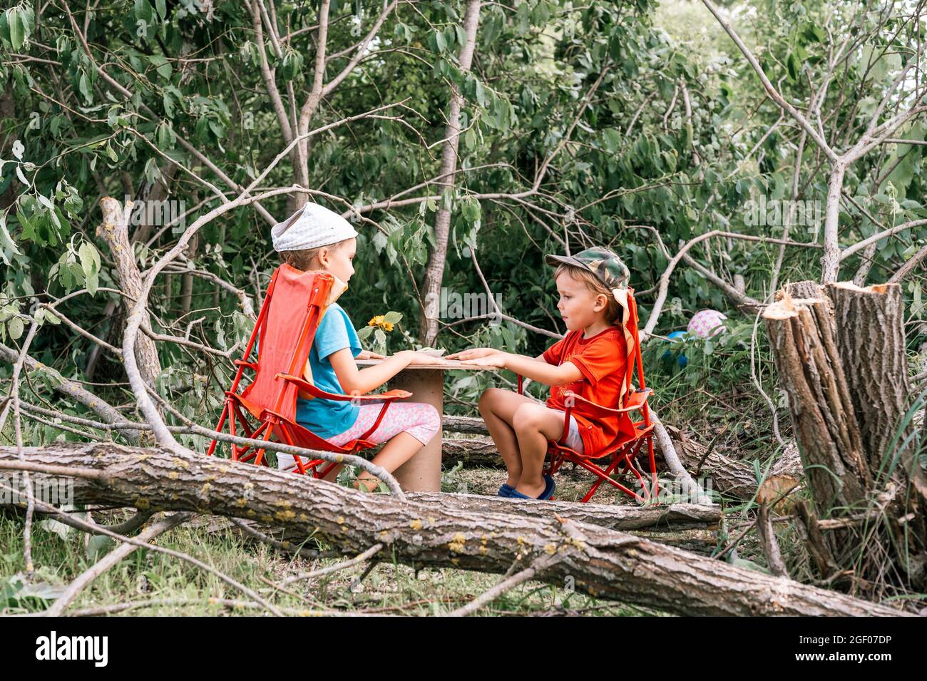 Russia, July 2020 - little kids, a boy and a girl friends have a fun picnic and eat among fallen trees in the summer in the village in the countryside Stock Photo