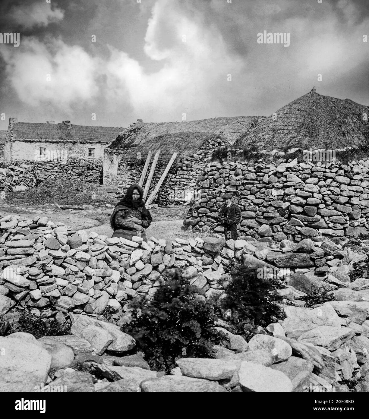 Woman and young boy in a lane next to Beehive huts in early 20th century Keel, Achill Island, County Mayo, Ireland Stock Photo