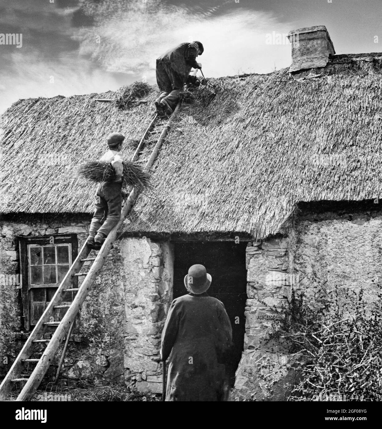 A thatcher and his young assistant on a cottage roof in early 20th century County Monaghan, Ireland Stock Photo