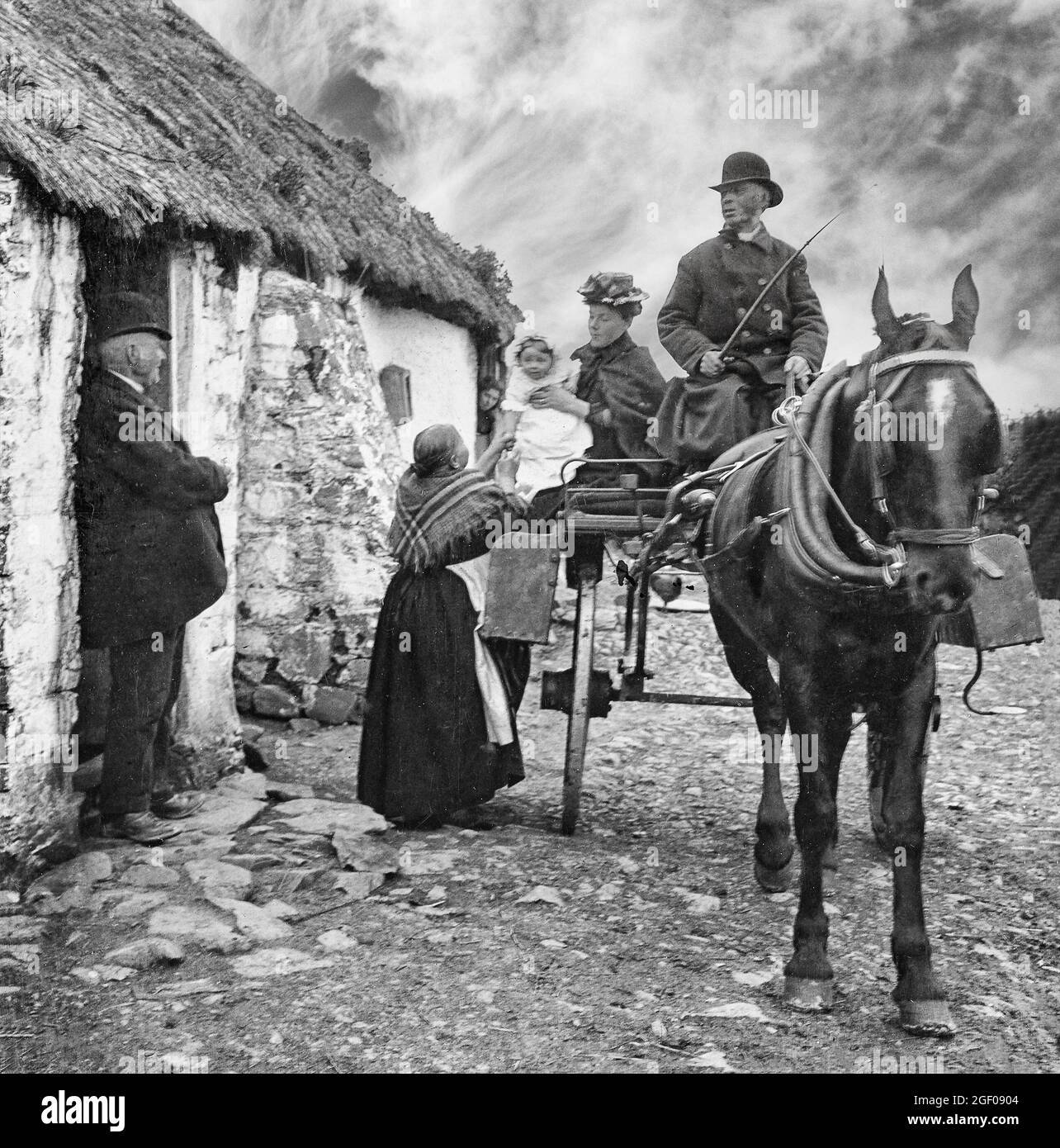 An early 20th century of family life as a grandmother reaches for her grandchild outside her cottage in County Monaghan, Ireland Stock Photo