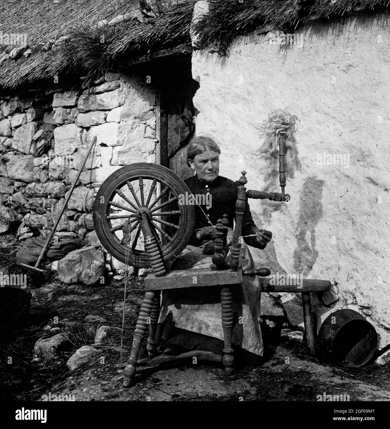 An early 20th century scene of a woman spinning flax outside her thatched cottage in Northern Ireland. Stock Photo