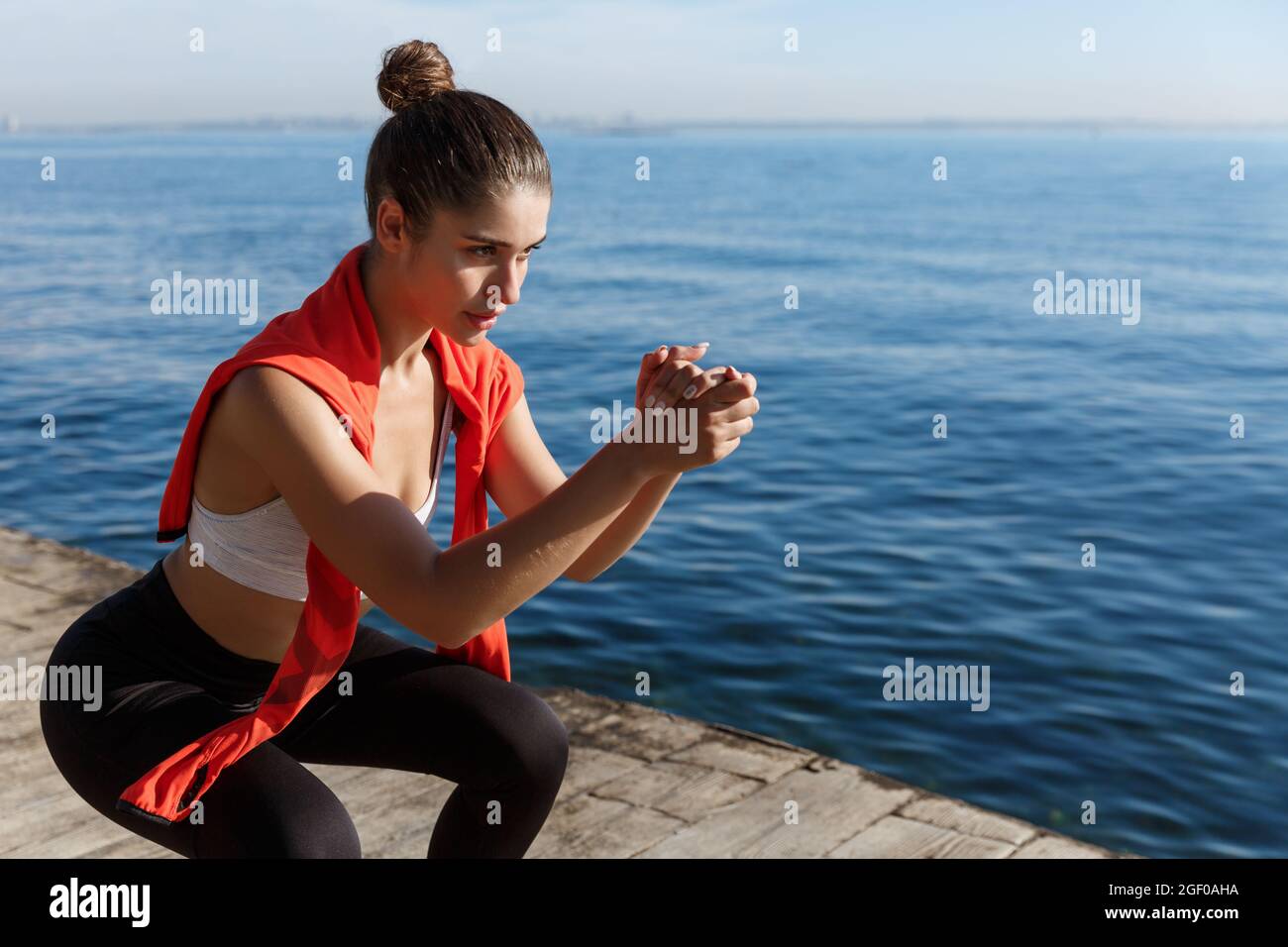 Side view of focused young sportswoman doing squats near the sea ...