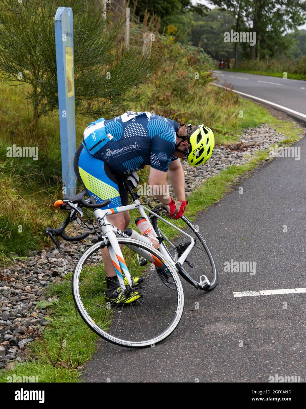 Fort Augustus, Scotland, UK. 22nd August, 2021. Cyclists taking part in the Etape Loch Ness closed road cycle sportive following a 360-degree 66-mile / 106-Km route around Loch Ness, Scotland, starting and finishing in Inverness. Thousands of pounds will be raised by participants for Macmillan Cancer Support, the official event charity. This image shows a participant making a quick repair near the half way point near Fort Augustus. Cliff Green/Alamy Stock Photo