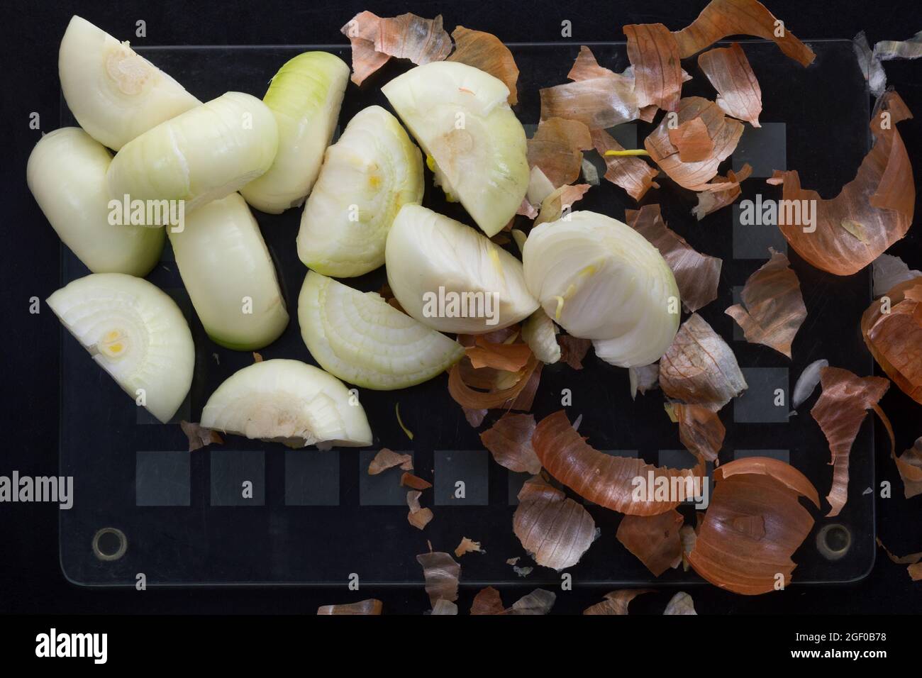 Top view of cut in half peeled onion and peels on black background ...