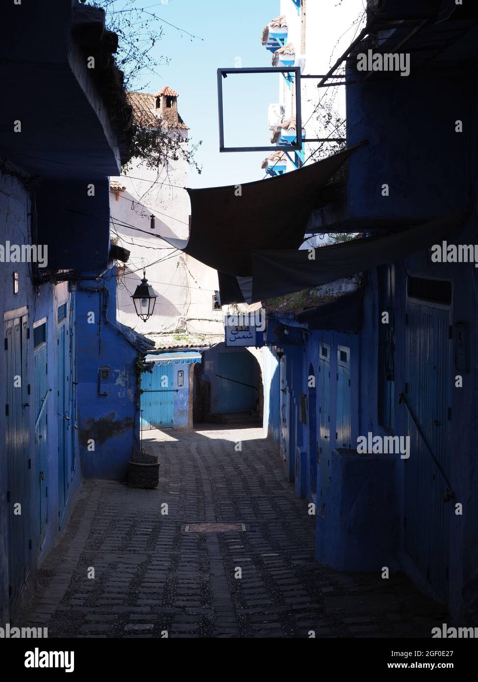 CHEFCHAOUEN, MOROCCO on APRIL 2019: Dark alley in african city, clear blue sky in warm sunny spring day - vertical Stock Photo