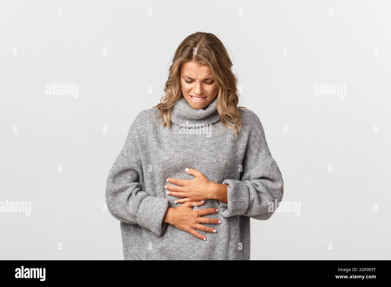 Portrait of blond girl feeling sick, touching stomach and grimacing