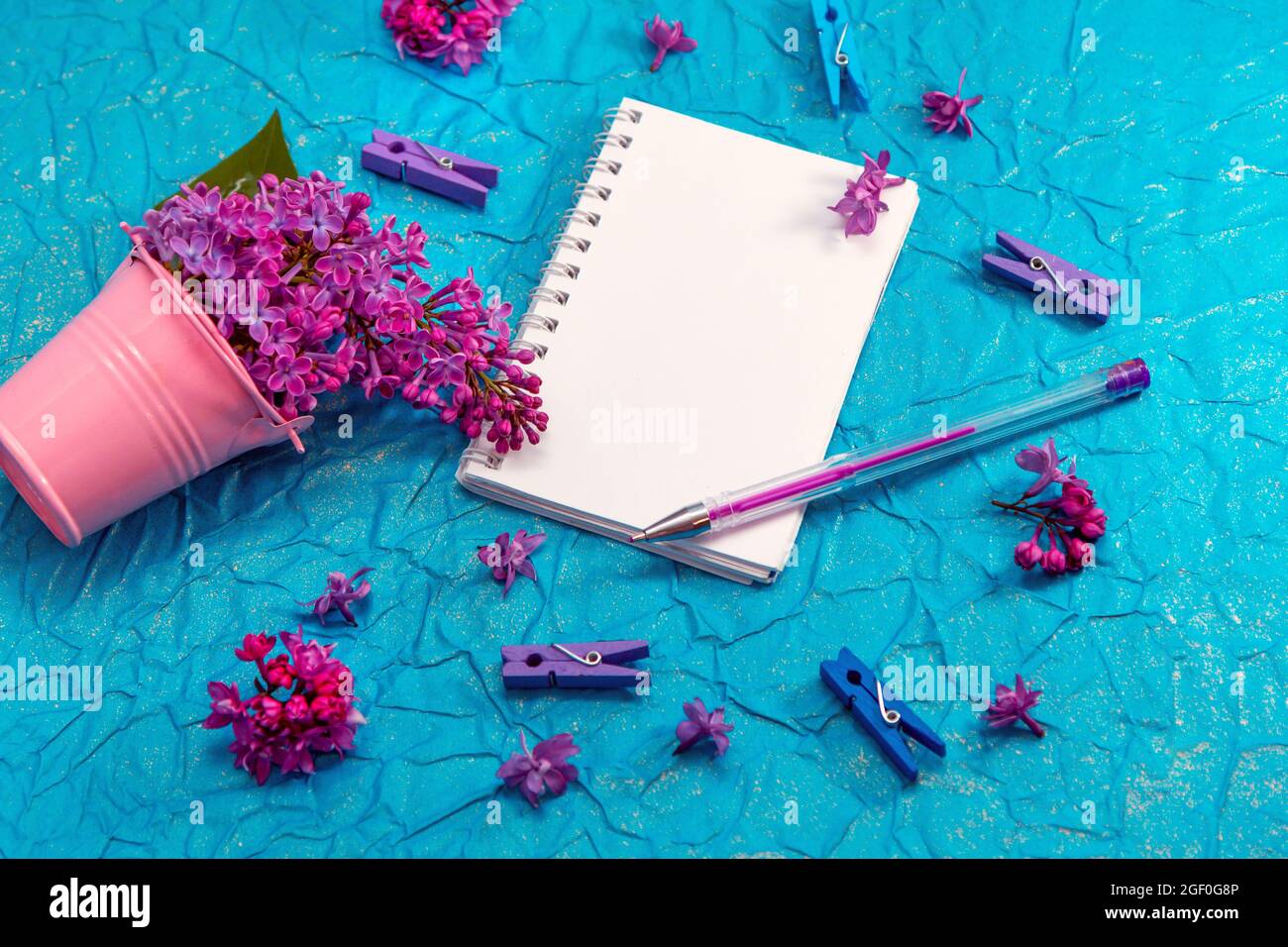 Blank notebook, pen with purple ink and lilac flowers on vintage painted blue cardboard background Stock Photo