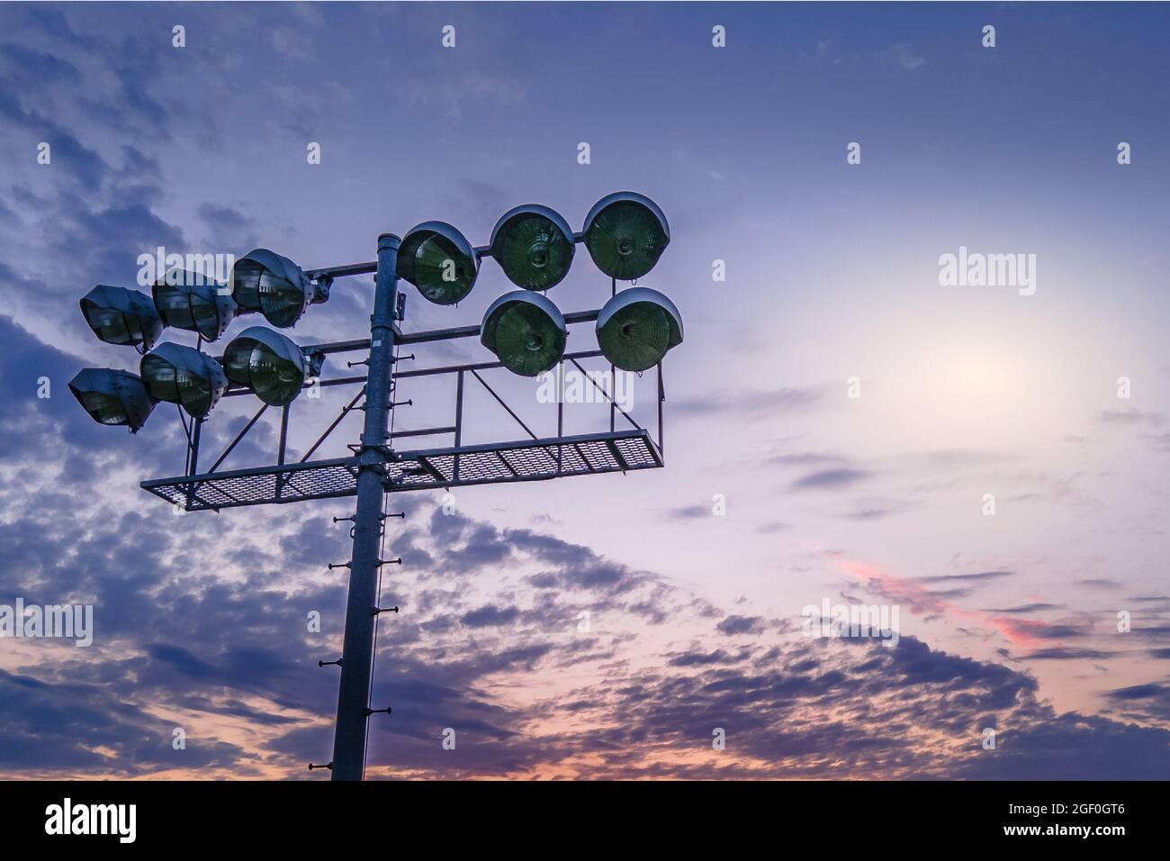 A beautiful golden hour sky with sport stadium lights in the foreground against a cloudy sky. Stock Photo