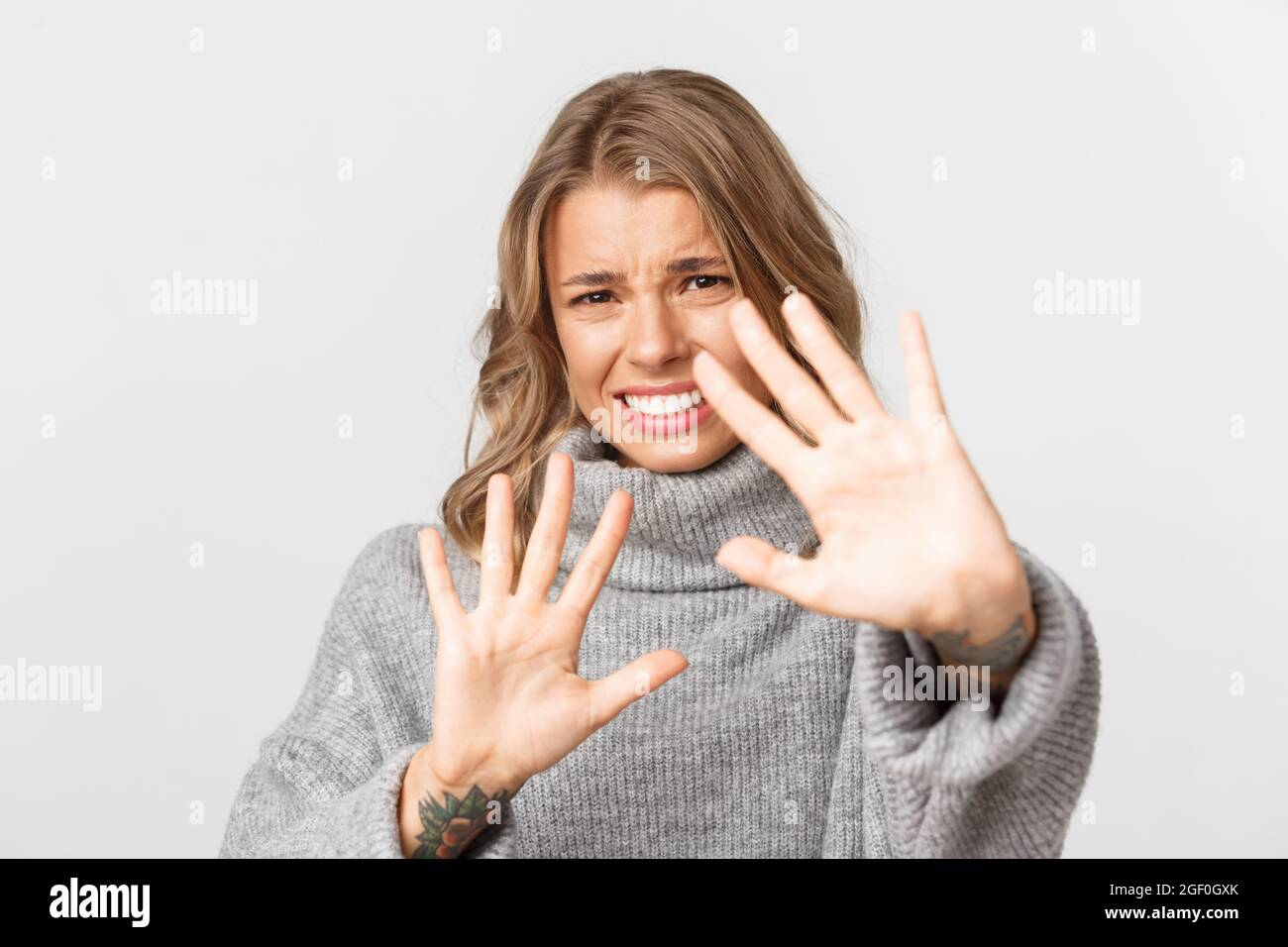 Close-up of bothered blond girl defending herself, grimacing from something disgusting or too bright, standing over white background Stock Photo