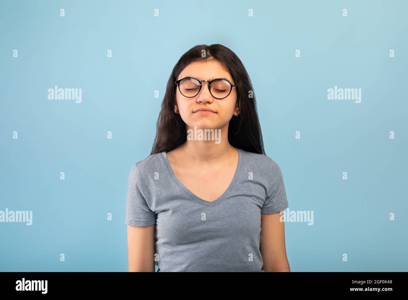 Calm Indian teen girl posing with closed eyes, meditating or praying to God over blue studio background Stock Photo