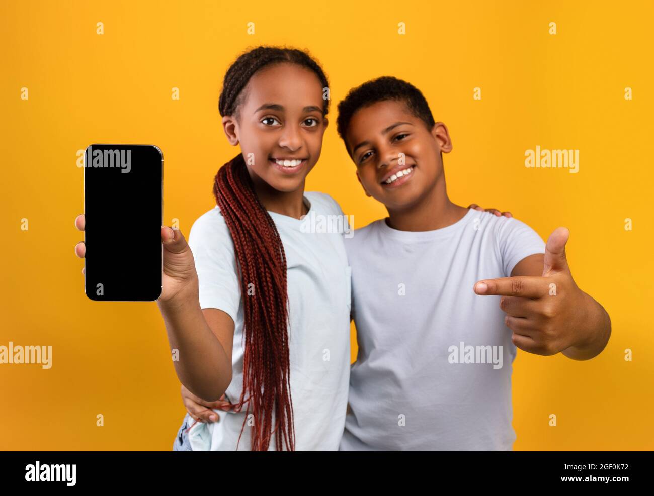 Adorable black teens brother and sister showing smartphone, mockup Stock Photo