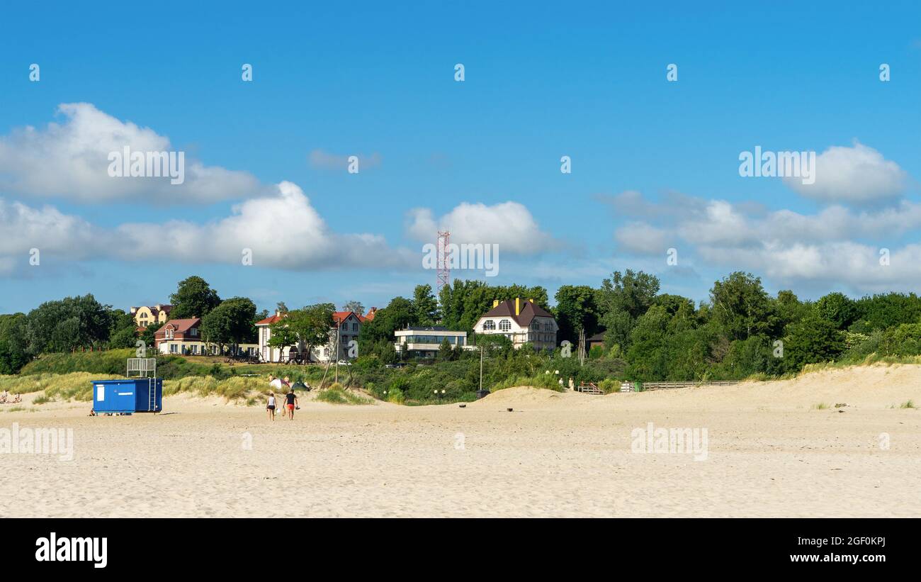 Public sandy beach in the village of Yantarny, Kaliningrad region, Russia. A man and a woman are leaving the seashore of Baltic sea in summer time. Stock Photo