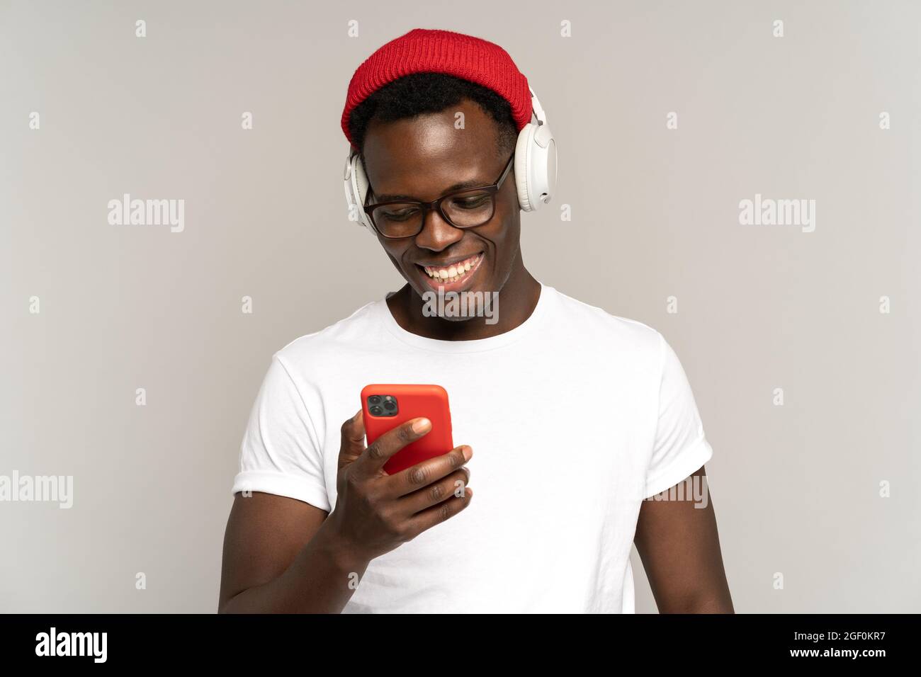 Black male listens to music in wireless headphones using social media in smartphone. Studio shot.  Stock Photo