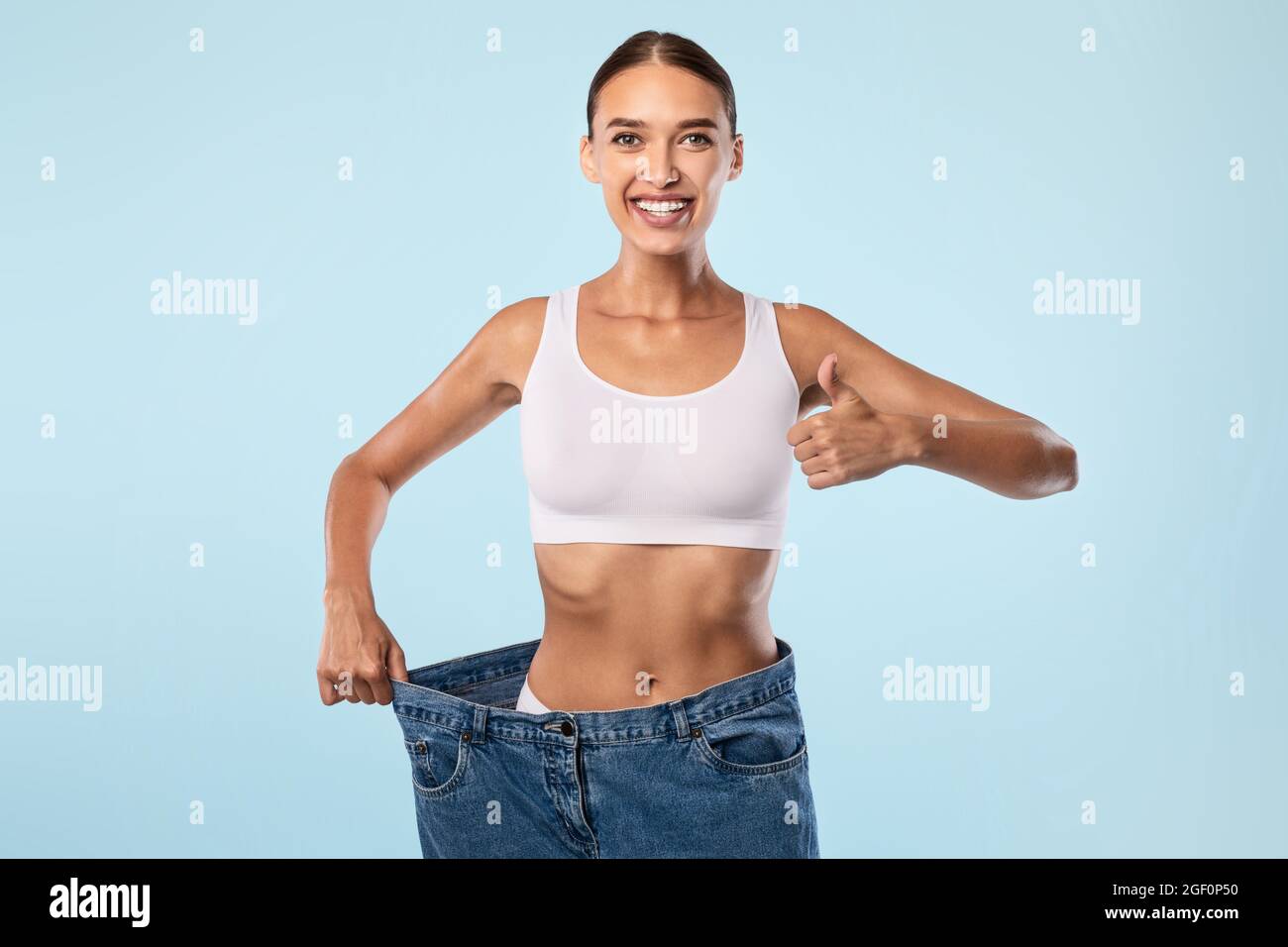 Woman Pulling Her Old Large Loose Jeans Showing Thumbs Up Stock Photo