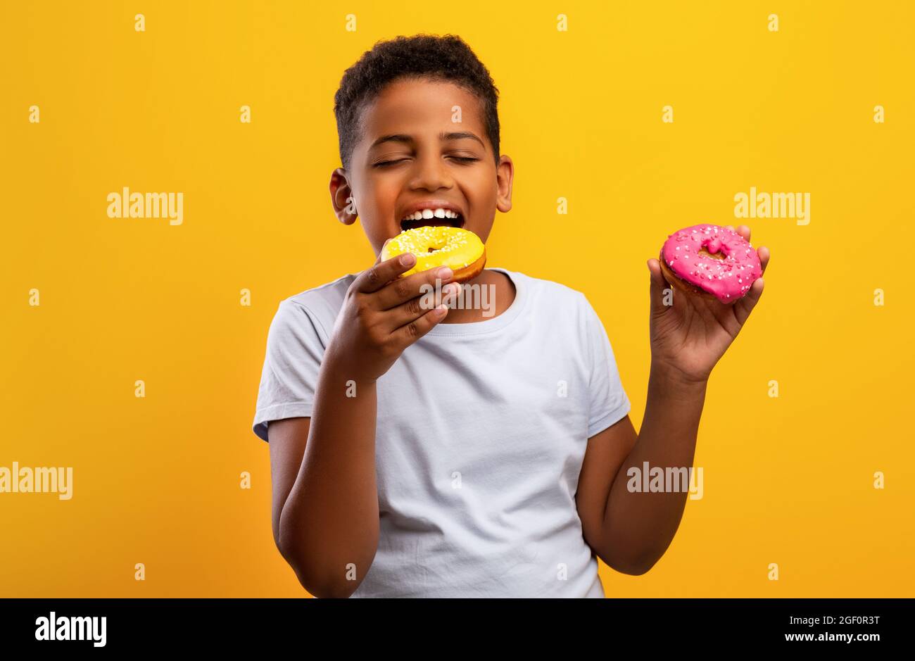 Black boy holding colorful donuts, isolated on yellow background Stock Photo