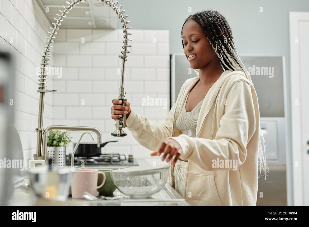 Portrait of young African-American woman washing dishes at home while doing chores on weekend, copy space Stock Photo