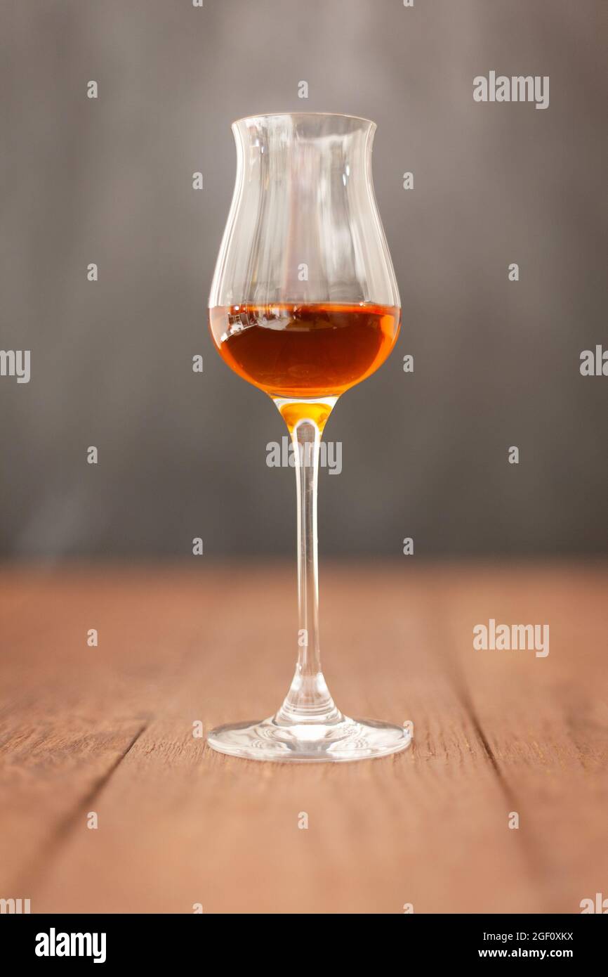 Grappa glass with brandy or sherry or calvados on wooden table with light grey background. Stock Photo