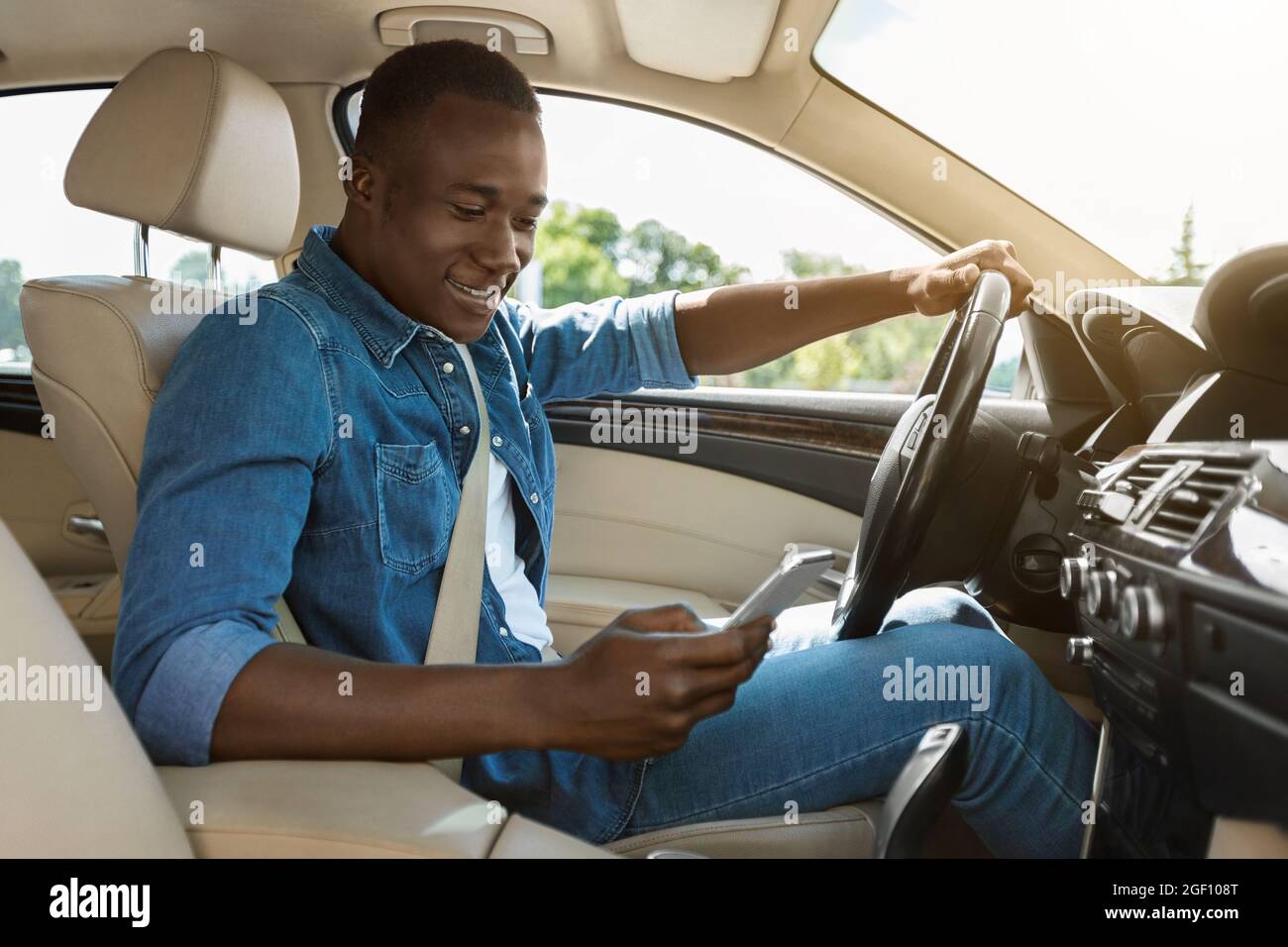 Smiling black guy using smartphone while driving car Stock Photo