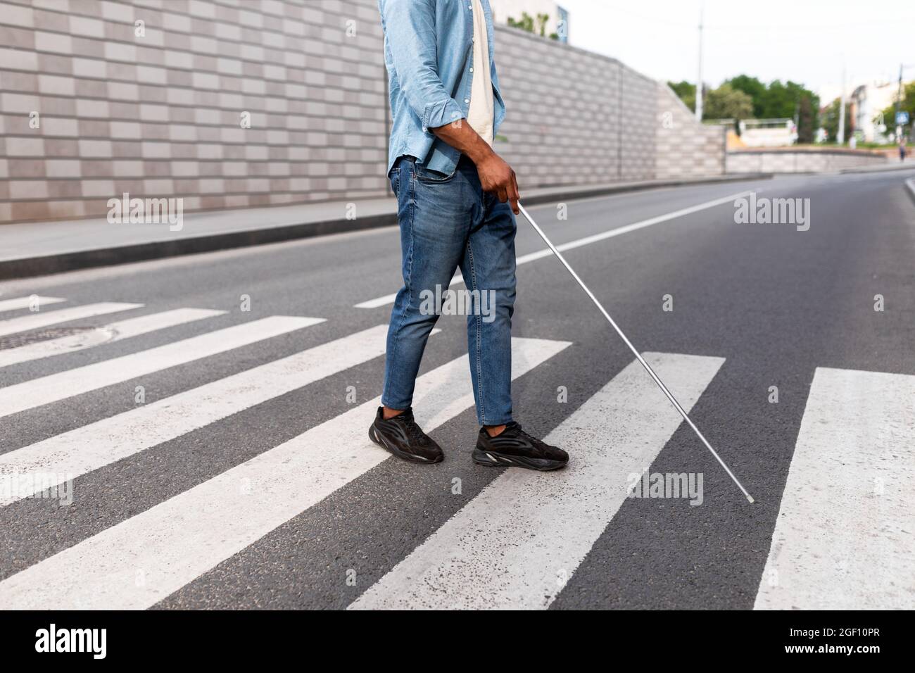 Unrecognizable young black visually impaired man with cane walking across city street, closeup Stock Photo