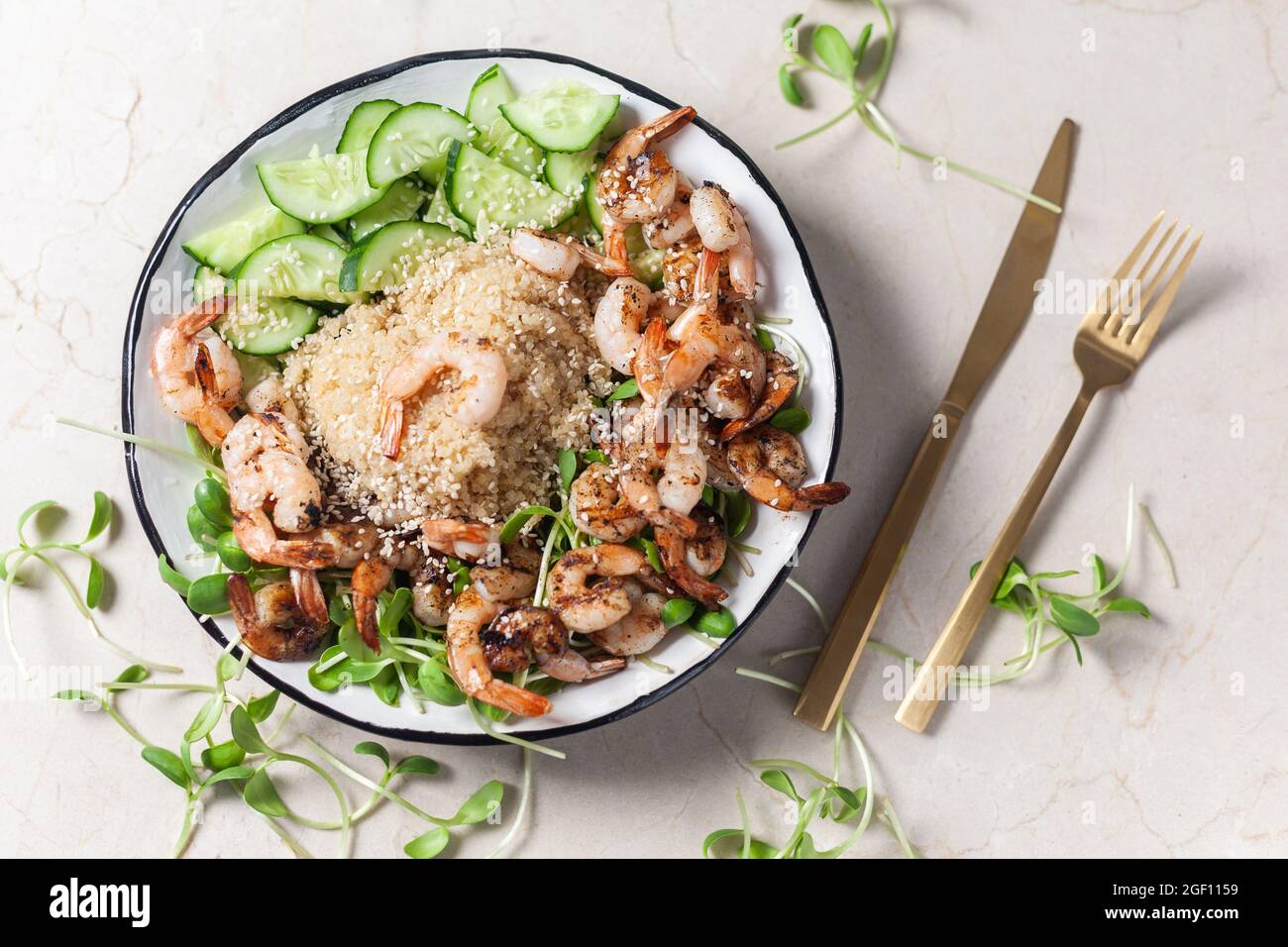 Quinoa with grilled prawns or shrimps, cucumber and micro greens on the marble background. Stock Photo