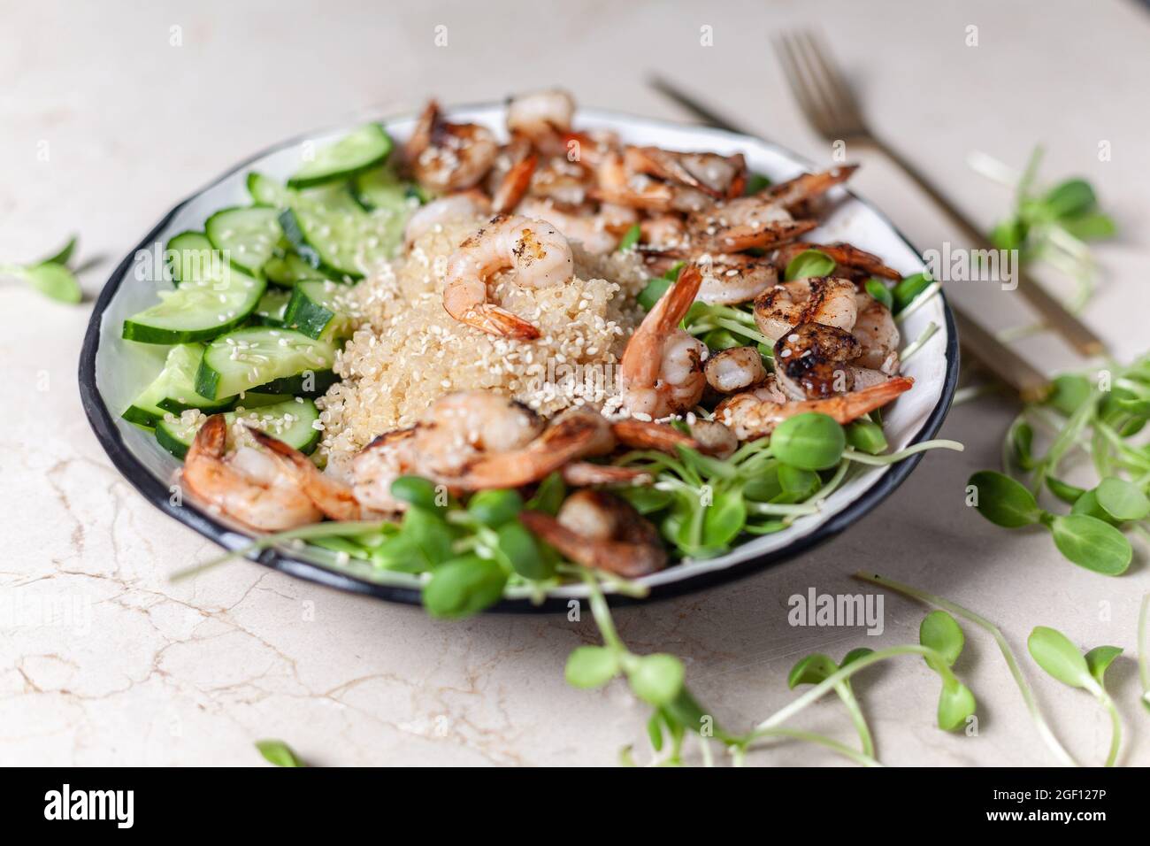 Quinoa with grilled prawns or shrimps, cucumber and micro greens on the marble background side view. Stock Photo