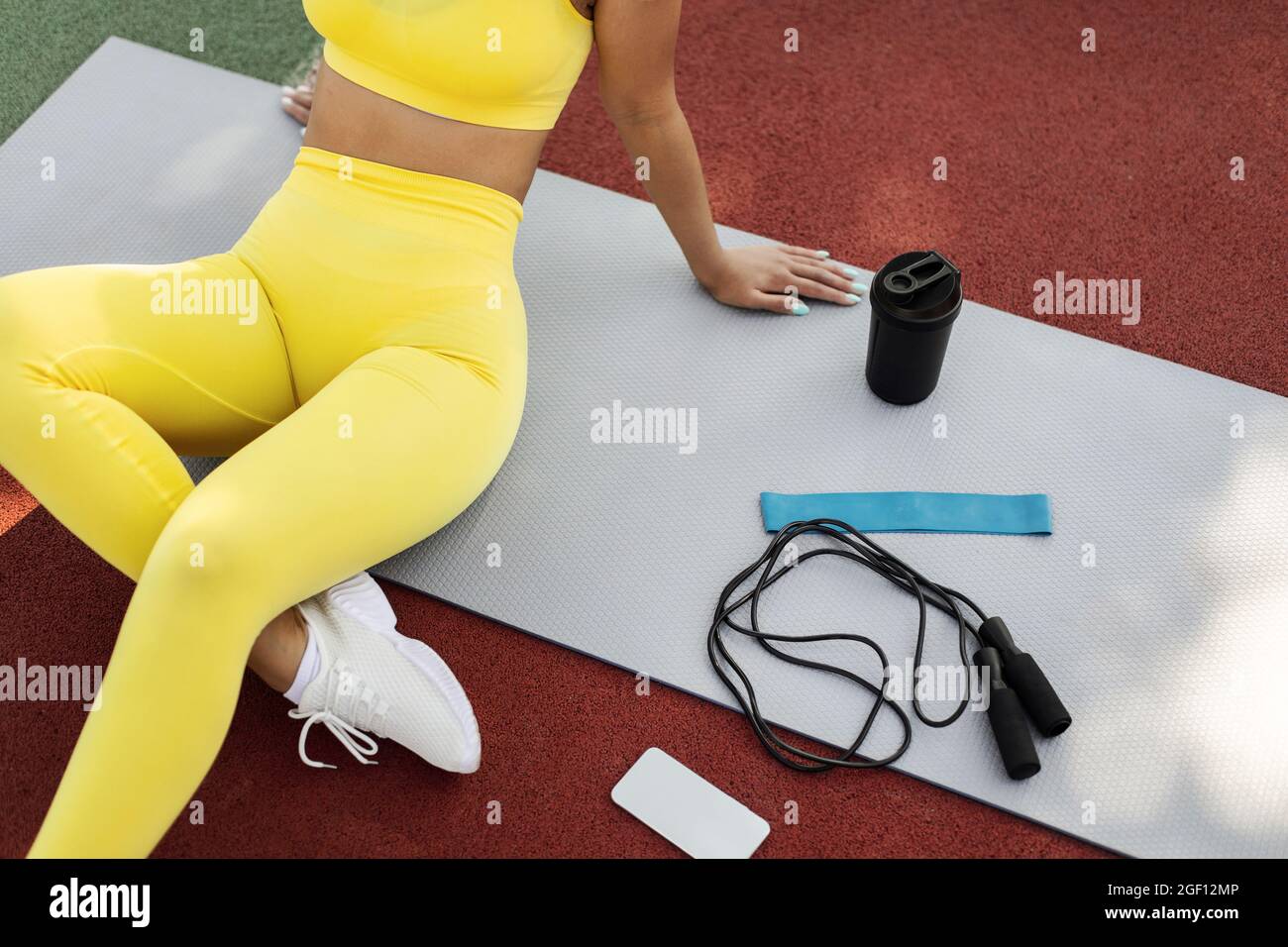 Black woman in yellow sportswear sitting on mat with equipment Stock ...