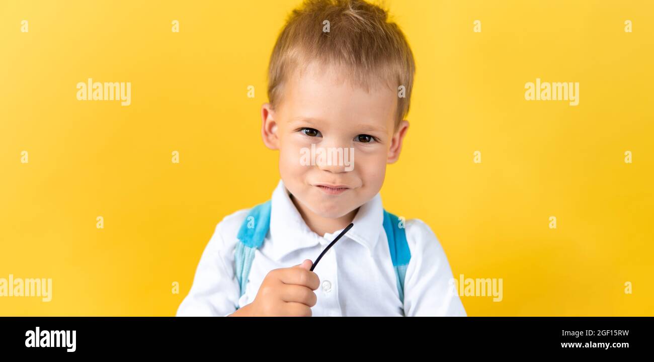 Banner Funny Preschool Child Boy smiles and looks slyly at camera on Yellow Background Copy Space. Happy Smiling Kid Go Back to School, Kindergarten Stock Photo